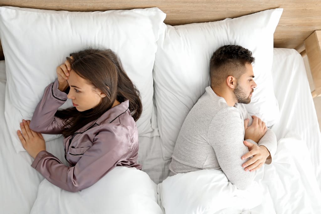 Kaksi ihmistä makaa sängyssä selät vastakkain valkoisten peittojen alla makuuhuoneessa