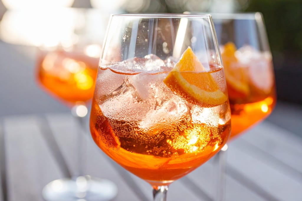 Oranssi spritz-juoma jääpaloilla ja appelsiiniviipaleella lasissa aurinkoisessa ympäristössä.