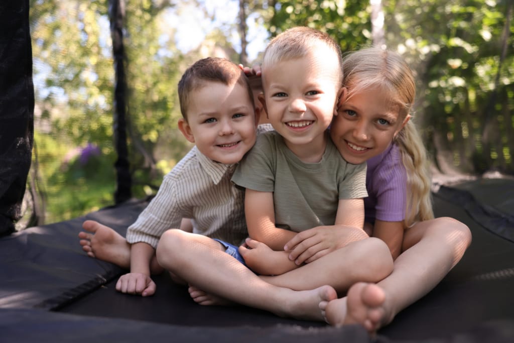 Kolme lasta nauraa ja leikkii ulkona lumessa kirkkaana talvipäivänä.