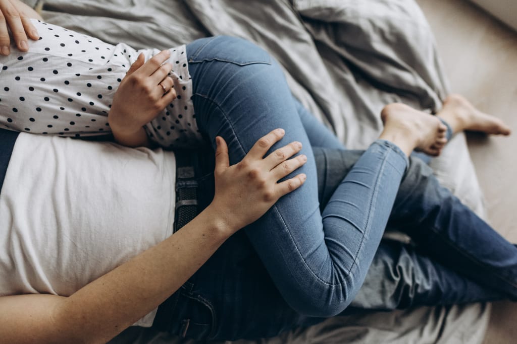 Kaksi aikuista makaa sängyssä kyljellään, toisen käsi lepää toisen reidellä