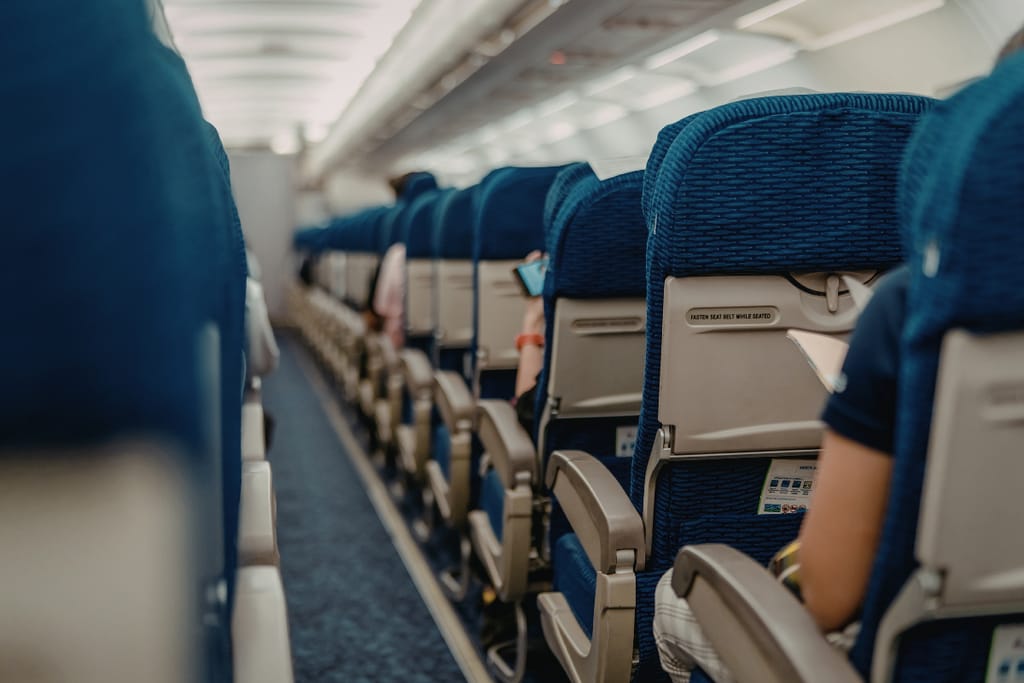 Lentokoneen matkustamo käytävältä kuvattuna, rivissä siniset istuimet ja matkustajia paikoillaan.