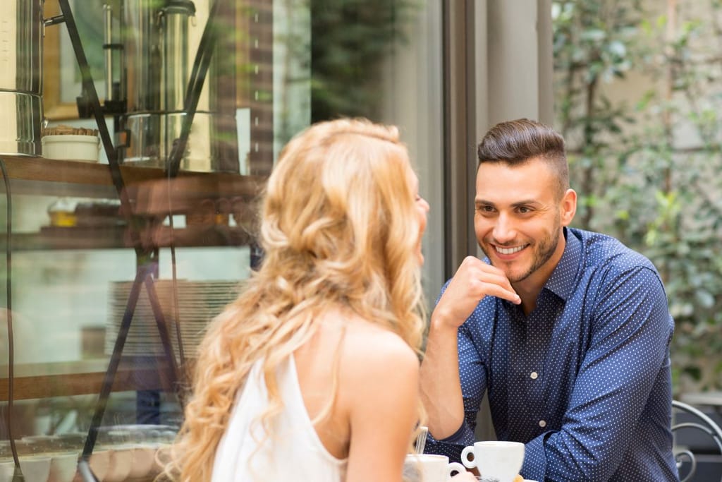 Mies ja nainen juttelevat kahvilassa kahvikuppien äärellä.