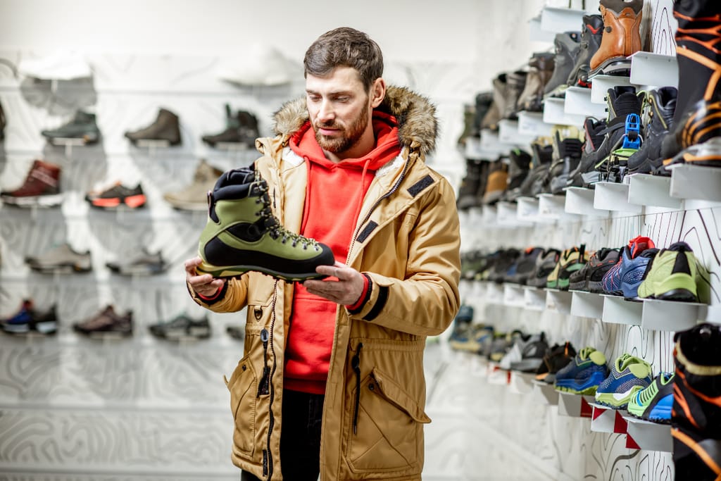 Mies tarkastelee vaelluskenkää urheilukaupassa, ympärillään esillä erilaisia kenkiä hyllyillä.