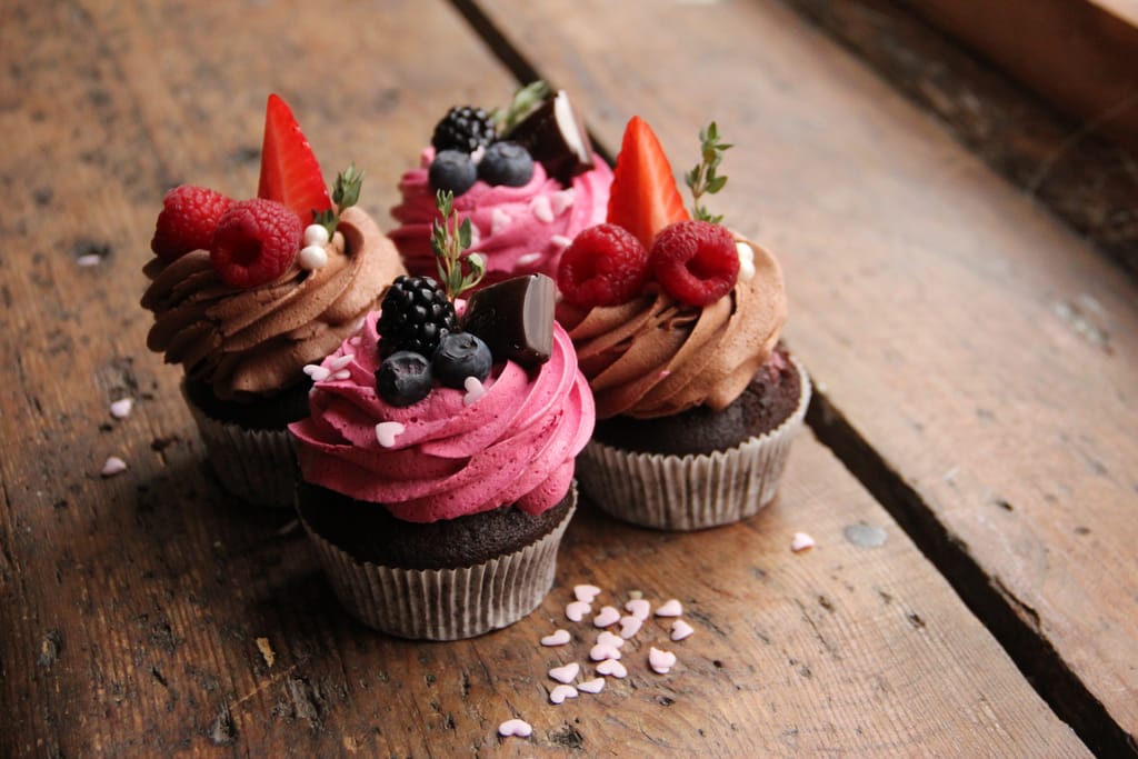 Vegaaniset suklaakuppikakut, joissa vaaleanpunainen ja ruskea kuorrute sekä tuoreita marjoja.