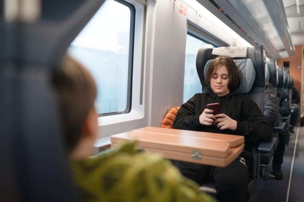 Lapsi istuu junan penkillä ja katsoo puhelinta pöydän ääressä matkustamon sisällä.