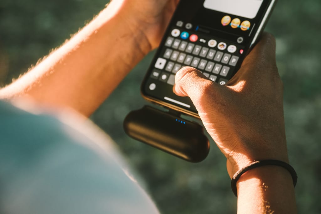 Kädet pitelevät älypuhelinta ja kirjoittavat viestiä, näytöllä näkyy emoji-näppäimistö.