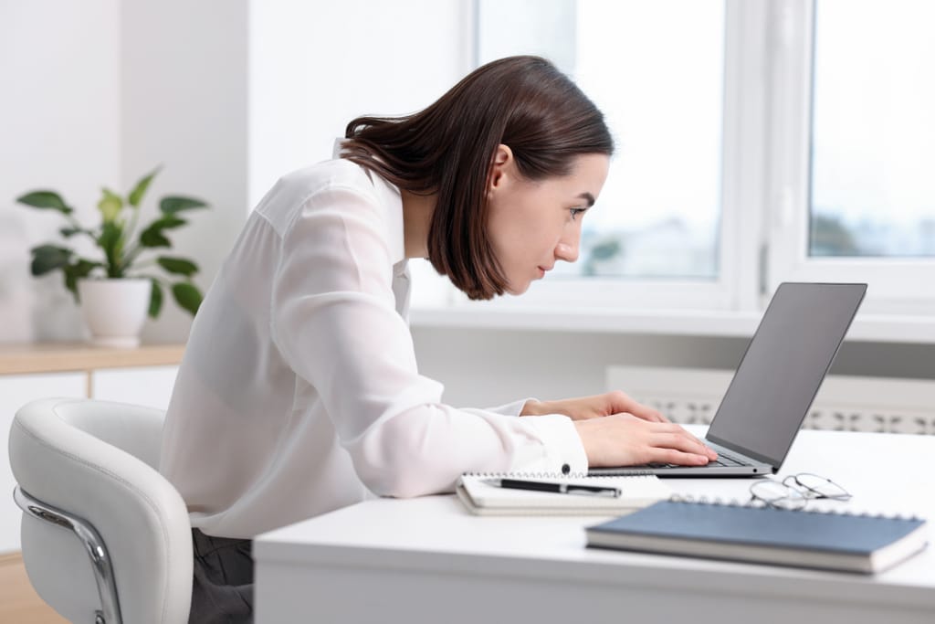 Aikuinen henkilö istuu työpöydän ääressä ja kirjoittaa kannettavalla tietokoneella ikkunan edessä