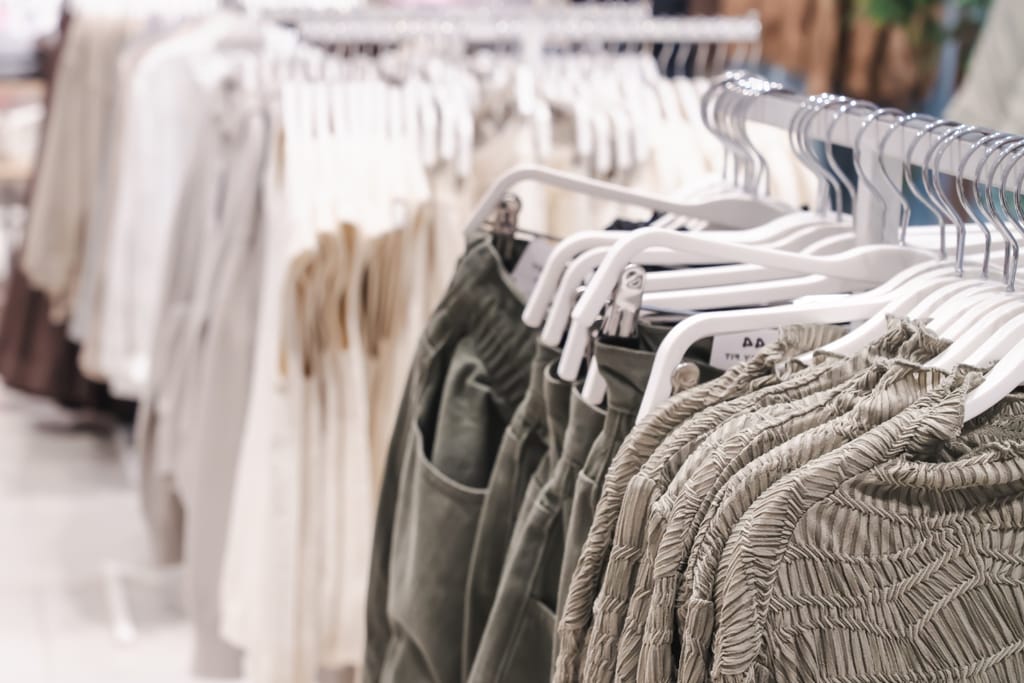 Vaaterekki, jossa vaaleita vaatteita ja housuja ripustimissa vaatekaupassa.
