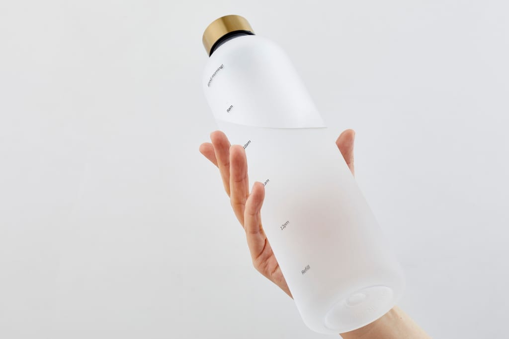 Käsi pitelee modernia, läpikuultavaa uudelleentäytettävää juomapulloa vaaleaa taustaa vasten.