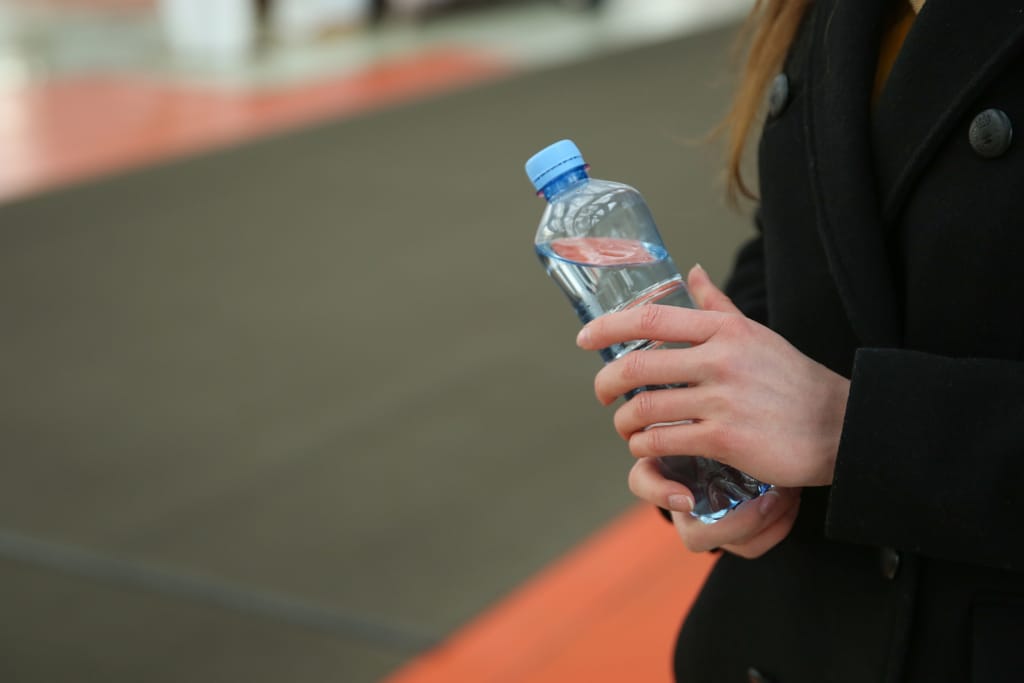 Henkilö pitää kädessään muovista vesipulloa julkisessa tilassa.
