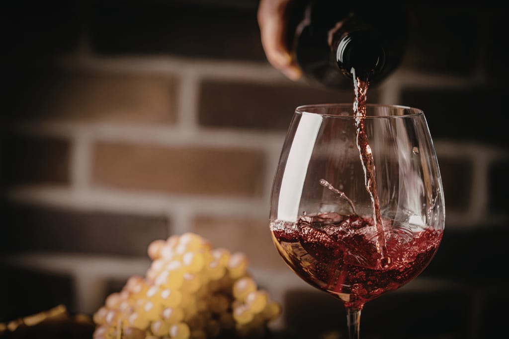 Punaviiniä kaadetaan lasiin. Taustalla tiiliseinä ja viinirypäleitä.