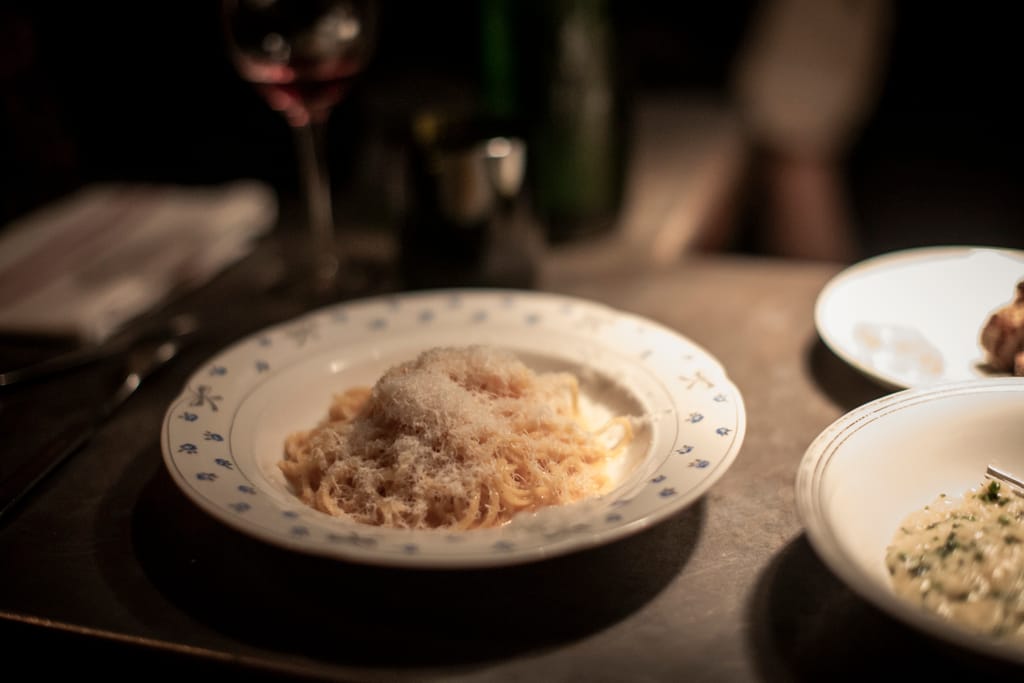 Pöydällä ravintola-annoksia. Lautasellinen pastaa, jonka päällä on parmesaania.