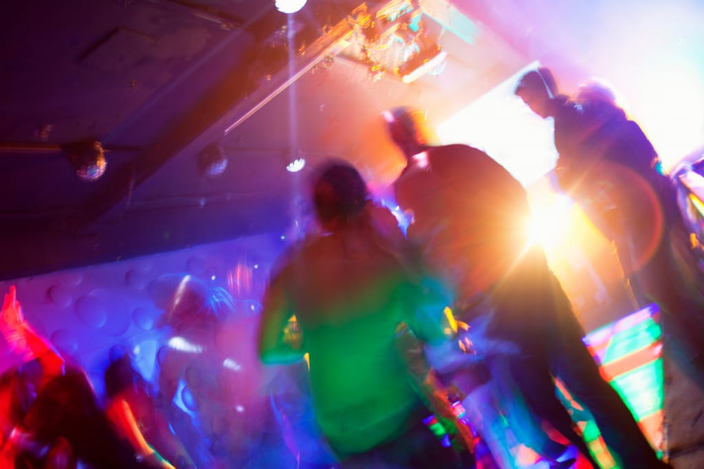 Ihmiset tanssivat klubilla värikkäiden valojen ja savuefektien keskellä.