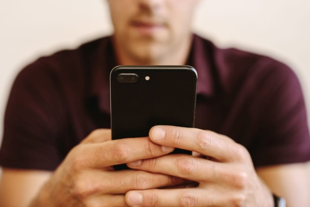 Mies selaa puhelinta kahvilassa ja hymyilee – rento hetki somessa