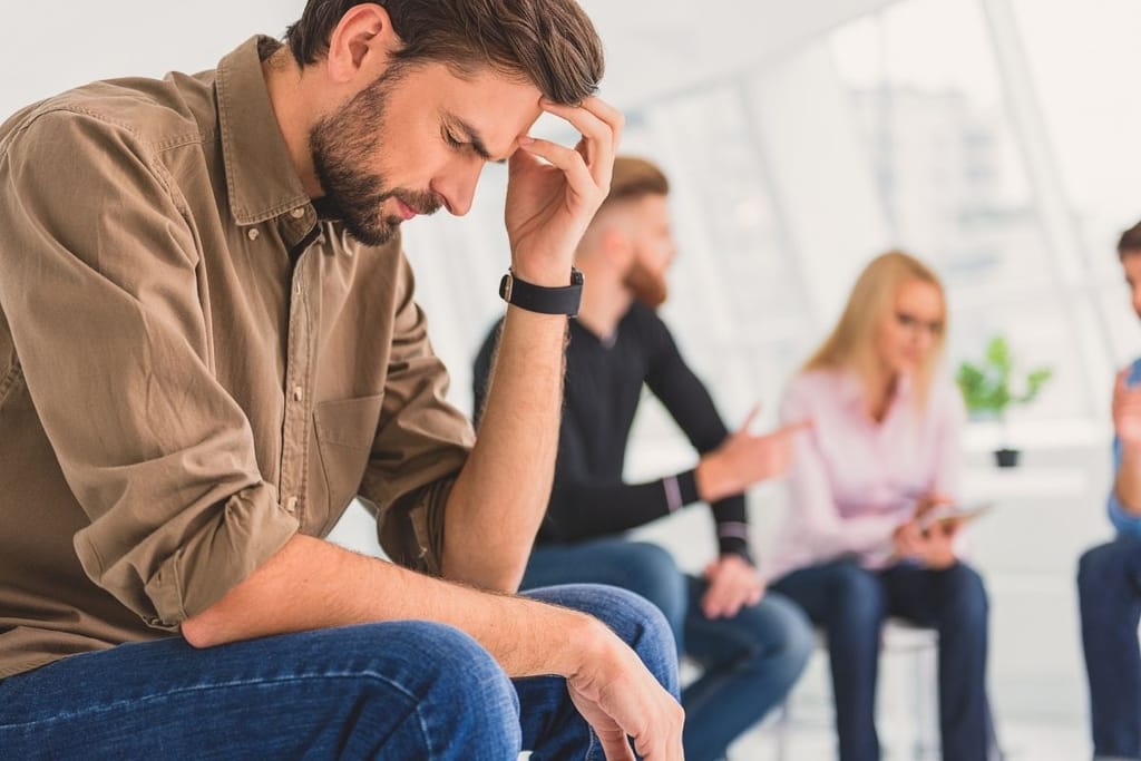 Mies stressaantuneena parisuhderiidan keskellä muiden riidellessä taustalla