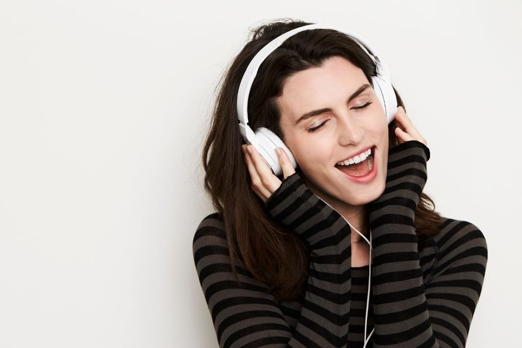 Nainen kuuntelee musiikkia kuulokkeilla silmät kiinni ja eläytyy voimakkaasti
