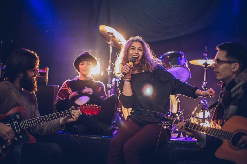 Nuori laulaja esiintyy hymyillen pienen bändin kanssa lavalla, taustalla rumpusetti ja kitaristeja.