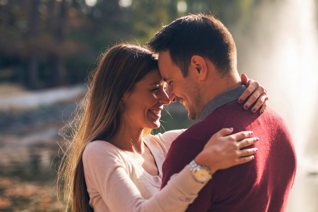 Rakastunut pariskunta halaa ja katsoo toisiaan hymyillen ulkona luonnon keskellä
