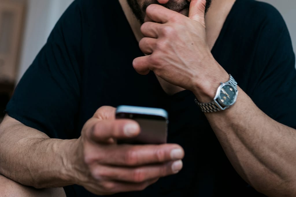 Mies katsoo puhelintaan mietteliäänä ja pitää kättä leuallaan.