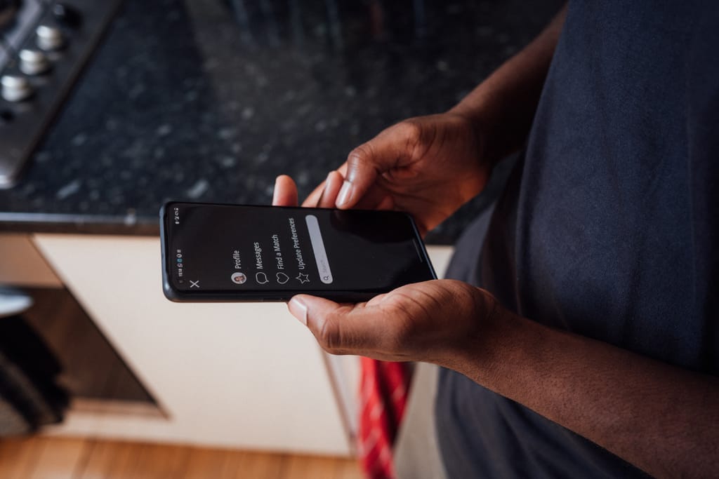 Henkilö käyttää puhelimessa treffisovellusta keittiössä.