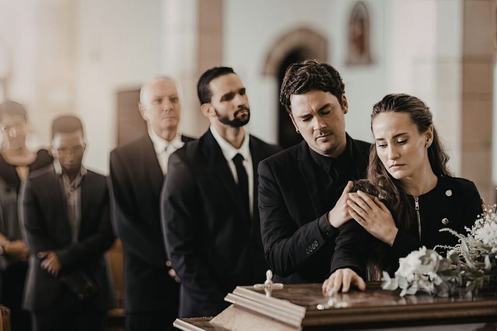 Surijat hyvästelemässä vainajaa kirkossa, nainen koskettaa arkkua miehen lohduttaessa