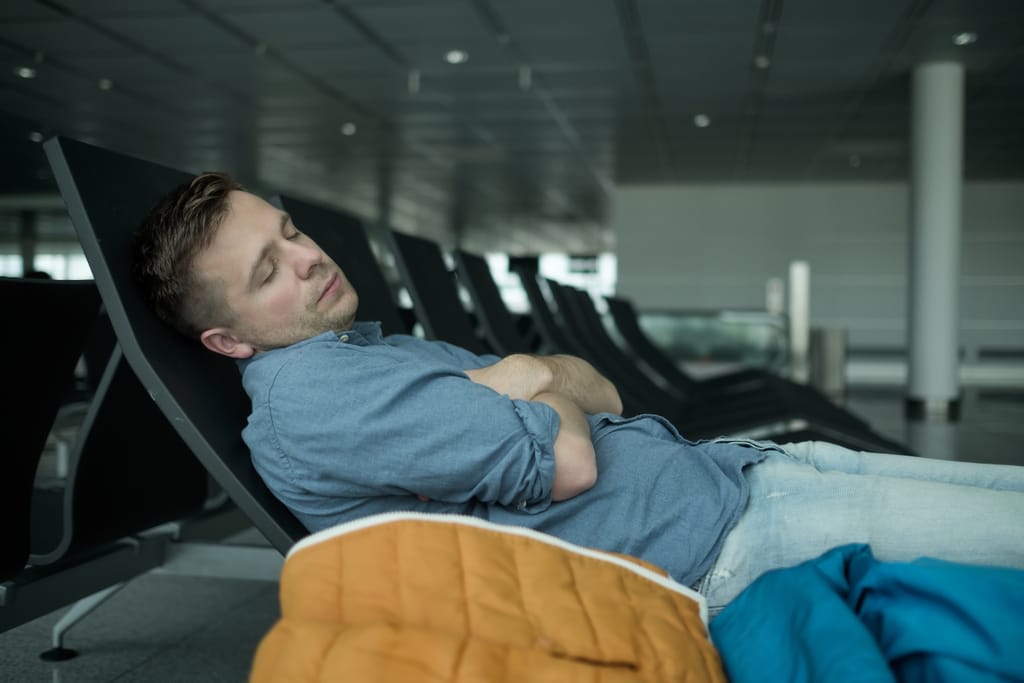 Mies nukkuu lentokentän penkillä vieressä takki.