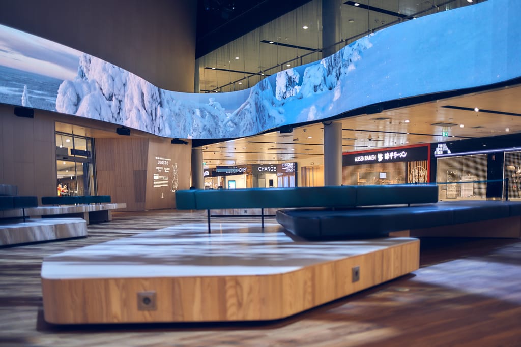 Lentokentän aula, istuinalue ja suuri näyttö seinällä.