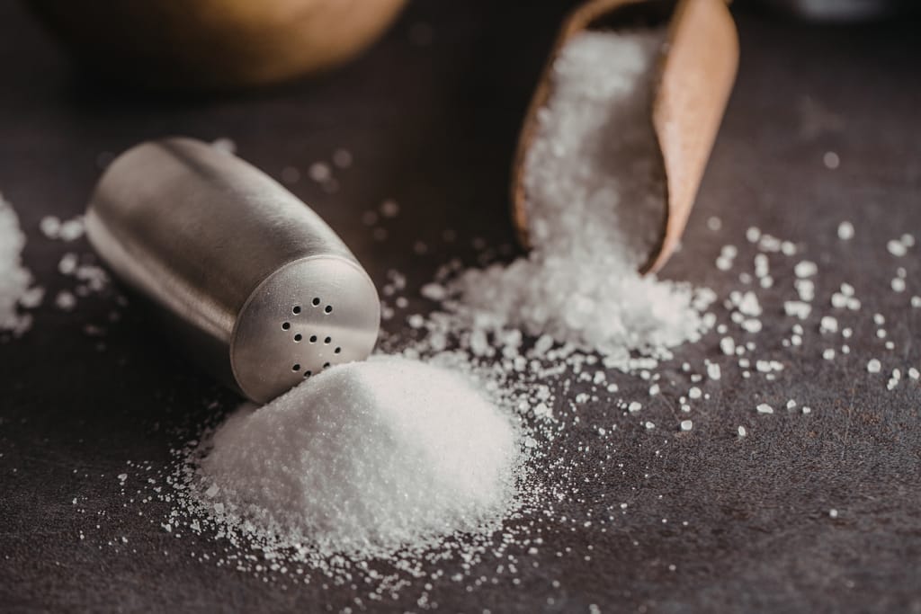 Suolaa kaadetaan puulusikasta pöydälle suolasirottimen viereen.