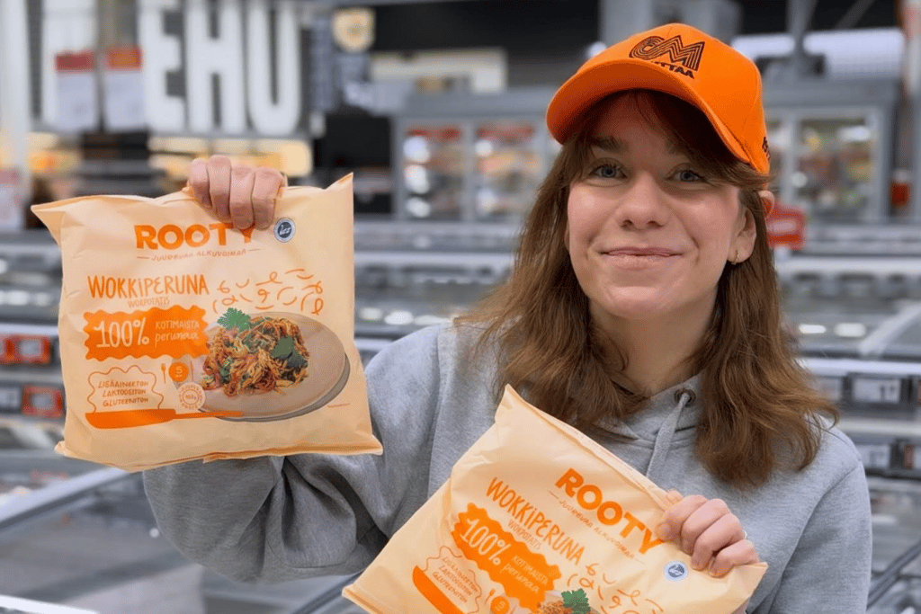 Henkilö seisoo kaupan pakastealtaan edessä ja pitelee käsissään kahta juurespohjaista pakasteperunatuotetta.