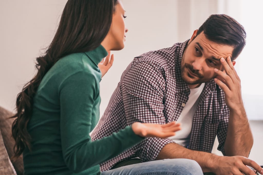 Nainen puhuu miehelle vakavana, mies kuuntelee ja pitää kättä otsallaan.