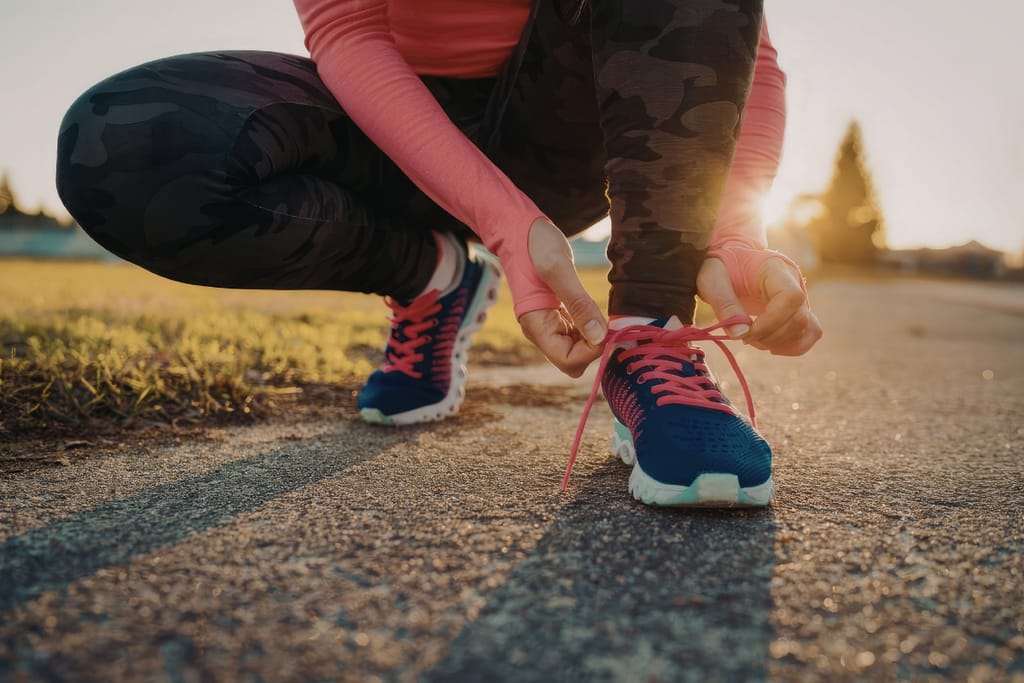 Nainen sitoo lenkkareita aamuauringossa.