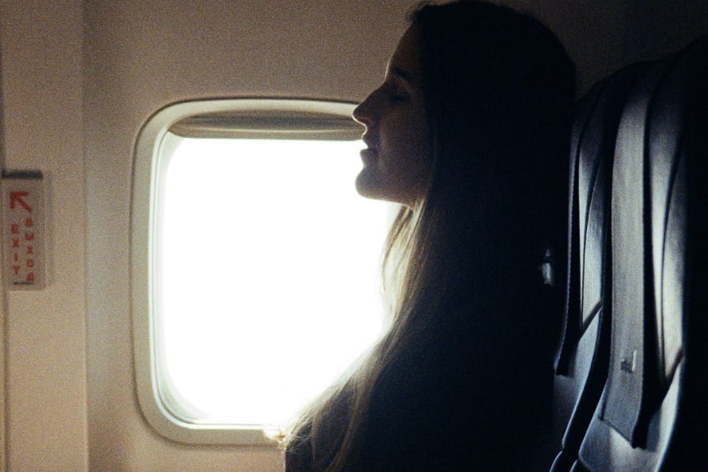 Nainen istuu lentokoneen ikkunapaikalla ja katsoo ulos kirkkaasta ikkunasta, kasvot sivuprofiilissa.