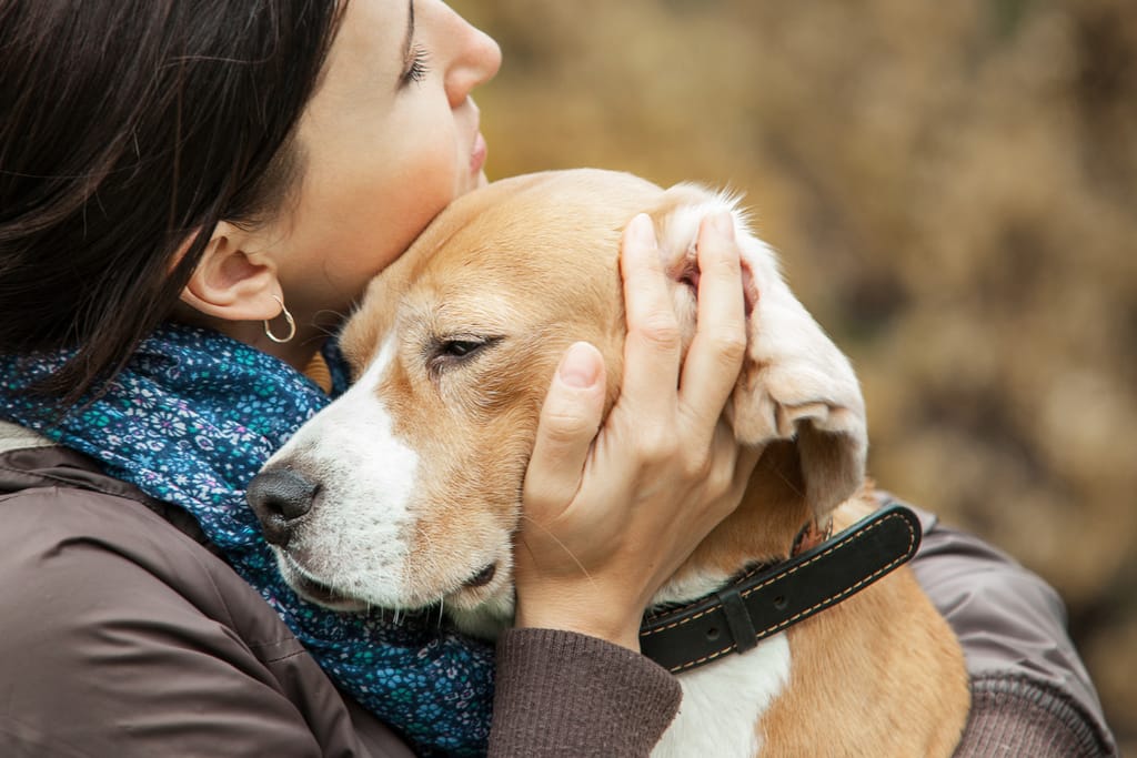 Nainen halaa ja suukottaa koiraa ulkona.