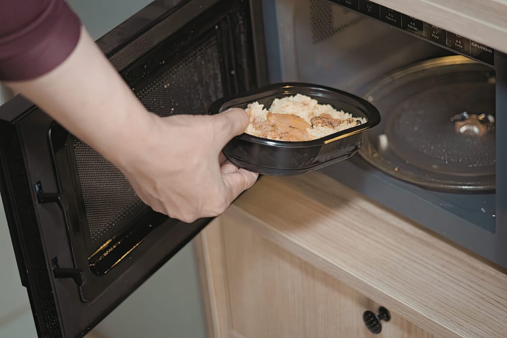 Mies laittaa valmisruokaa mikroaaltouuniin.