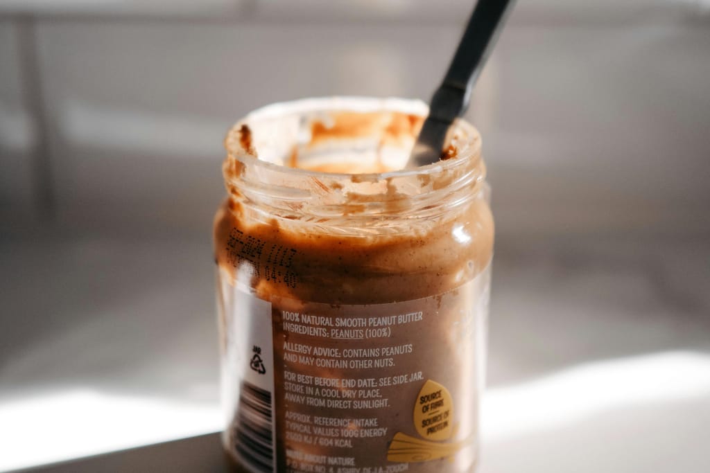 Avattu maapähkinävoipurkki, jossa lusikka ja purkin reunoilla kahvimainen vaahtoisa juomaseos.