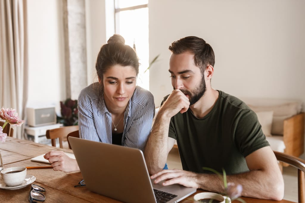 Nainen ja mies katsovat yhdessä kannettavan tietokoneen näyttöä kotona työpöydän ääressä.