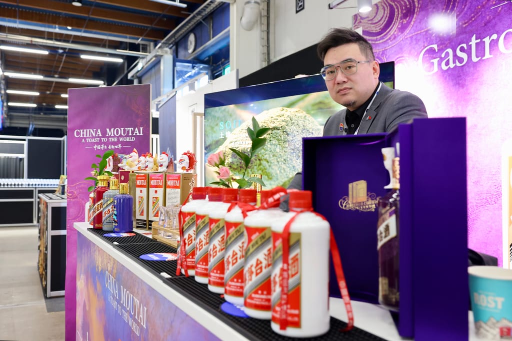 Mies esittelee China Moutai -juomia messuosastolla, etualalla pulloja ja pakkauksia.