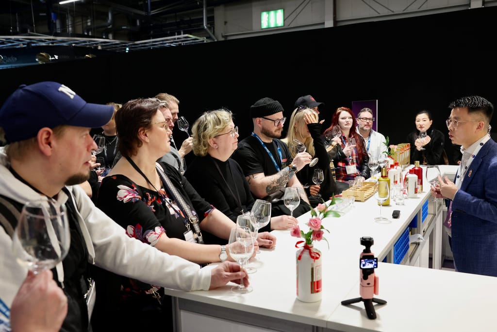 Ryhmä ihmisiä maistaa juomia tiskin äärellä messuilla esittelijän johdolla.
