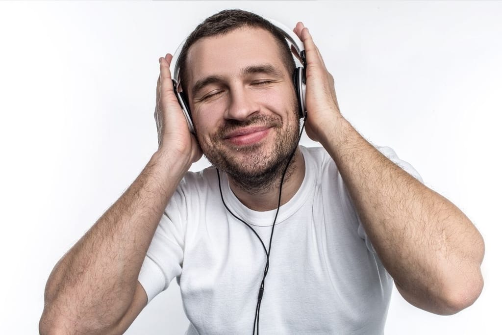 Mies kuuntelee musiikkia kuulokkeilla silmät kiinni ja hymyilee