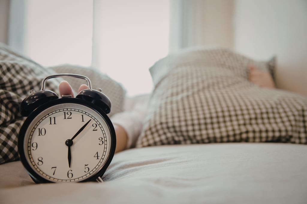 Kuva makuuhuoneesta. Etualalla herätyskello ja takana petaamaton sänky.