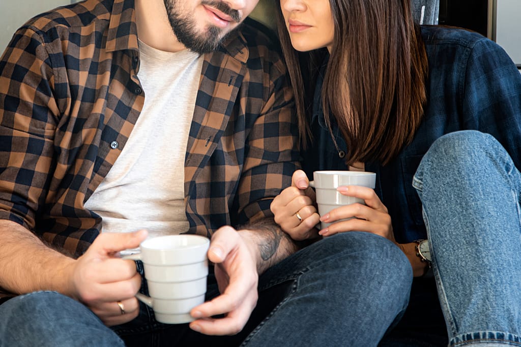 Pariskunta istuu vierekkäin kahvikupit käsissään ja keskustelee.