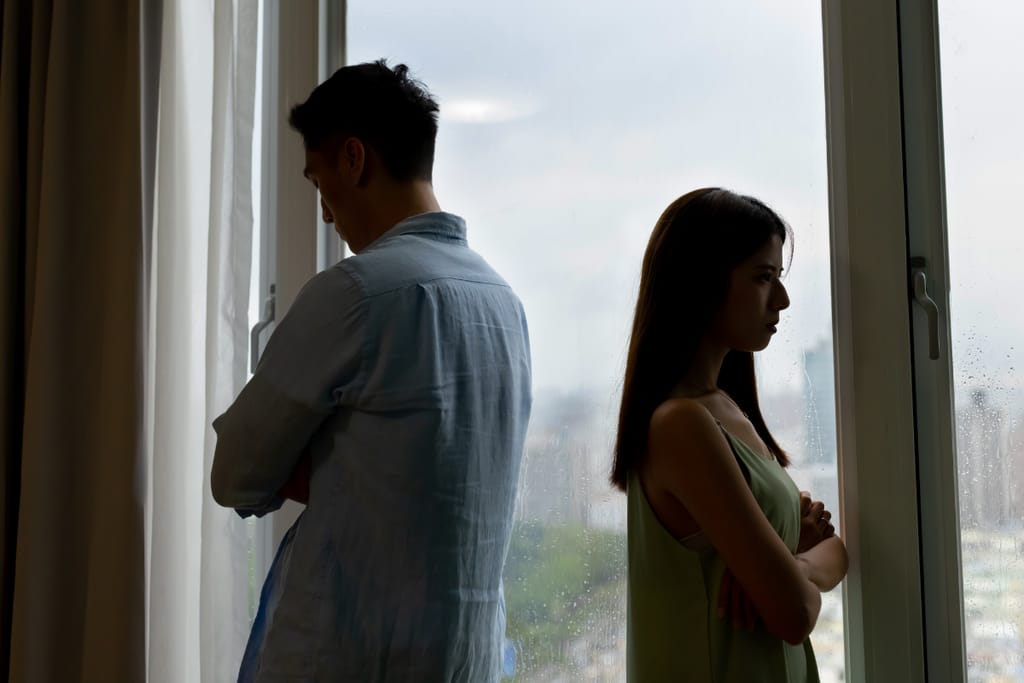 Mies ja nainen seisovat selät vastakkain ikkunan edessä riidan jälkeen.