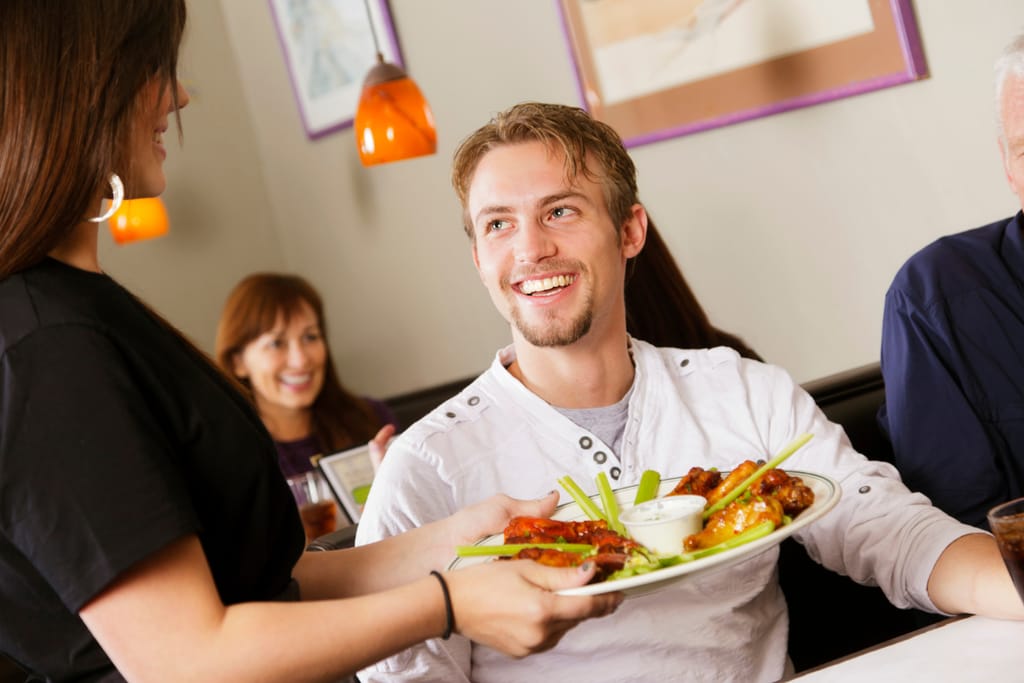 Asiakas hymyilee tarjoilijalle, joka tuo annosta pöytään.