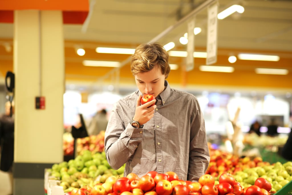 Poika haistelee omenaa ruokakaupassa.