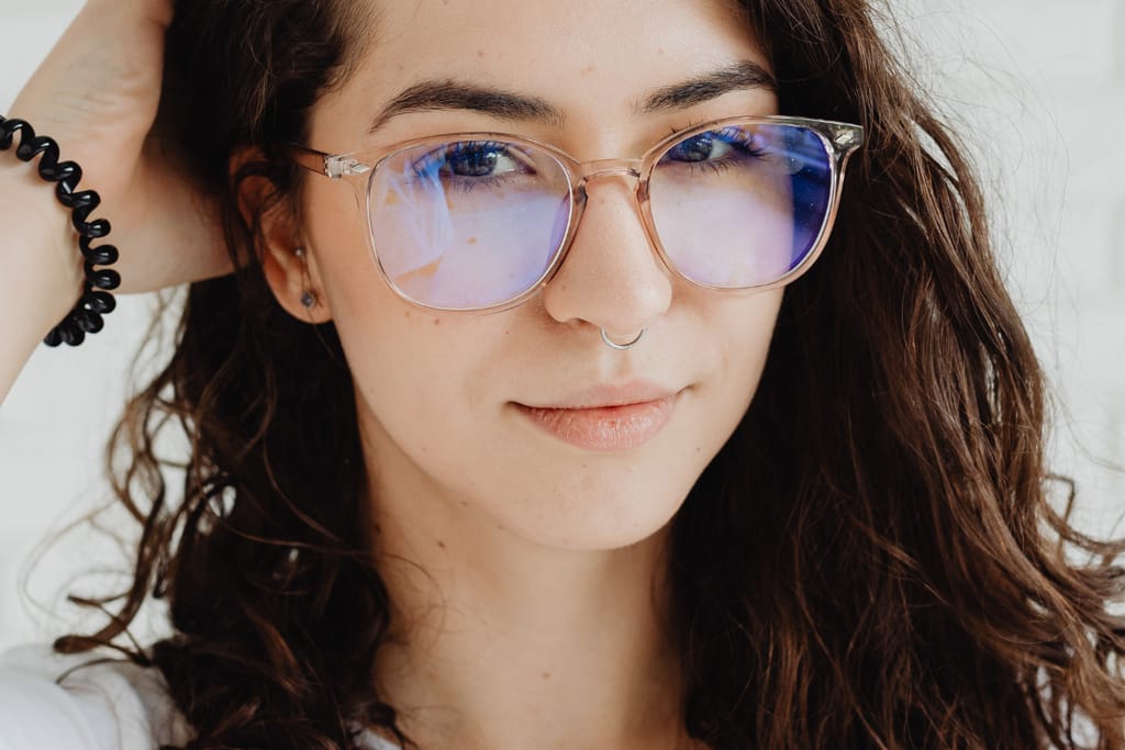 Nainen käyttää silmälaseja ja katsoo kameraan lähikuvassa.