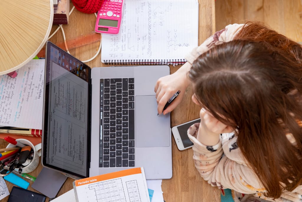Ylhäältä kuvattu työskentelytilanne, jossa henkilö käyttää läppäriä paperien ja muistiinpanojen keskellä.