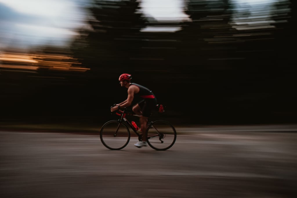 Maantiepyöräilijä ajaa kovaa vauhtia hämärässä, tausta liikkeessä sumentunut.