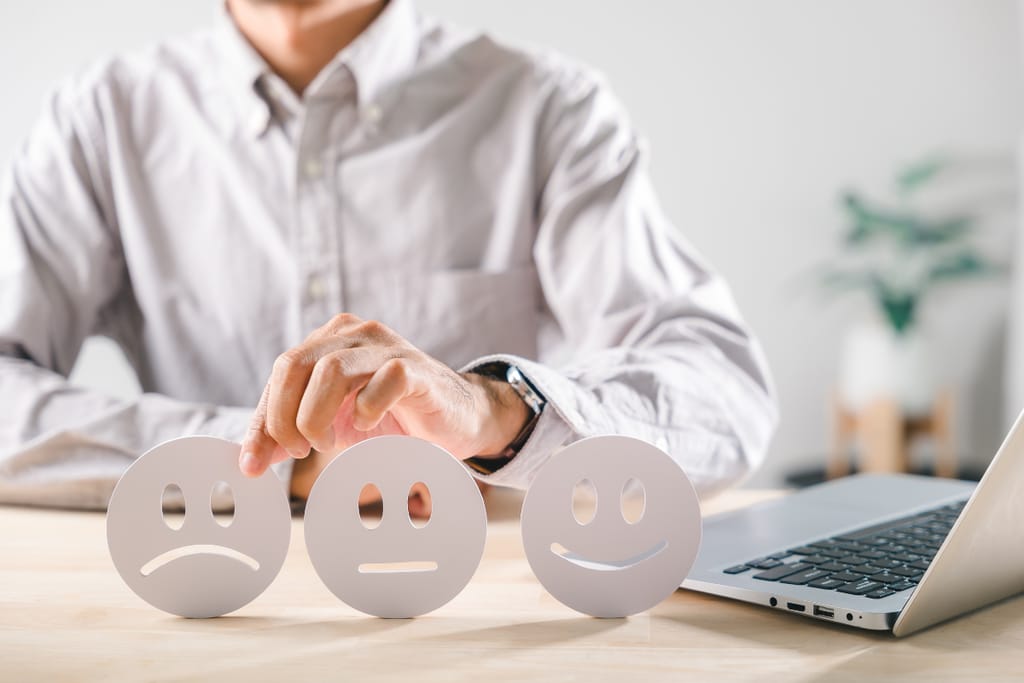 Henkilö valitsee tyytyväisyysikonien joukosta neutraalia kasvoa pöydällä, kannettava tietokone vieressä.