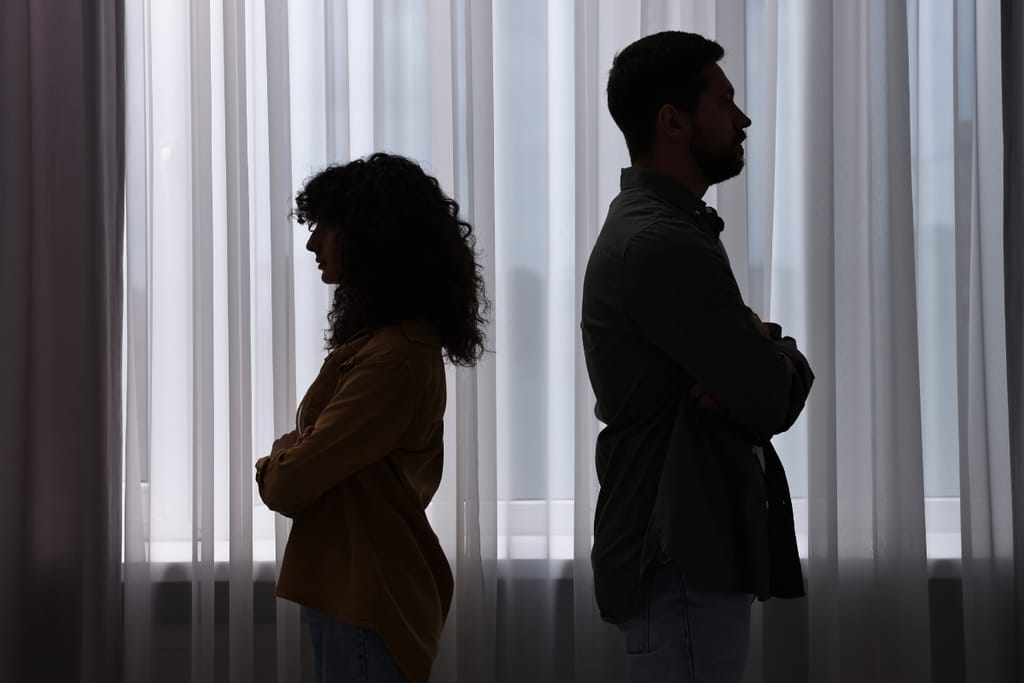 Mies ja nainen seisovat selät vastakkain kädet puuskassa ikkunan edessä.