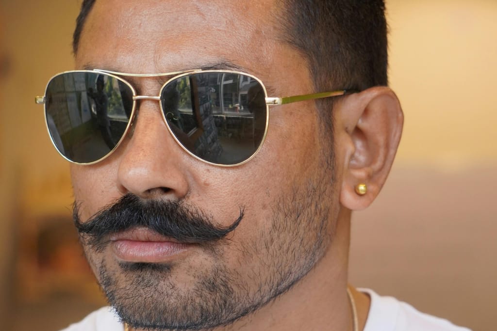 Mies aurinkolaseissa, tuuheat viikset ja korvakoru.